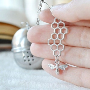 May include: Silver tea infuser with a honeycomb design and a small bee charm. The infuser is attached to a chain.