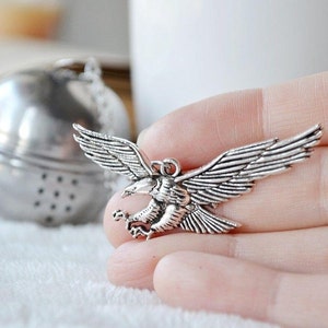 May include: Silver tea infuser with a detailed eagle design. The eagle is in flight with its wings spread wide. The infuser is attached to a chain.