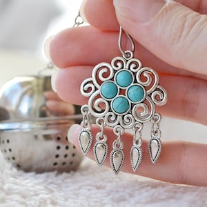 May include: Silver dangle earrings with a turquoise stone design. The earrings feature a floral pattern with five turquoise stones and dangle charms.