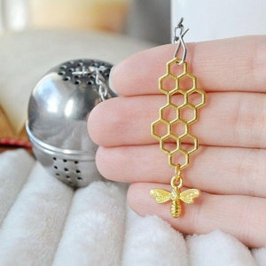 May include: Gold honeycomb tea infuser with a small bee charm. The infuser is attached to a silver chain and ball.