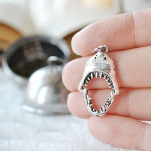 Puede incluir: Encanto de diente de tiburón de plata con un diseño detallado. El encanto está abierto y muestra los dientes afilados del tiburón.