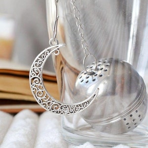 May include: Silver tea infuser with a crescent moon shaped handle. The infuser is a ball with small holes and is attached to a chain.