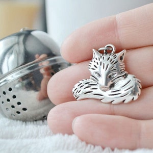 May include: Silver fox tea infuser charm. The fox is curled up with its tail wrapped around its body.