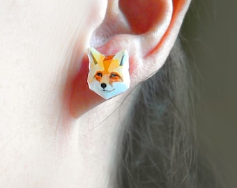 Könnte beinhalten: Nahaufnahme eines Ohrs mit einem geometrischen Fuchsohrstecker. Der Ohrring hat ein Fuchskopf-Design mit orange, weißen und schwarzen Farben. Der Ohrring ist ein kleines, dekoratives Accessoire.