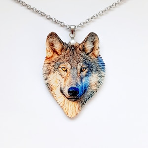 Op de afbeelding: Een ketting met hanger met een gedetailleerde wolfskop. De hanger toont een realistisch wolfsgezicht met bruine, grijze en blauwe tinten en gele ogen. De ketting heeft een zilverkleurige ketting.