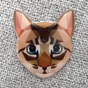 Peut inclure: Un autocollant en forme de chat avec un design géométrique. L'autocollant représente le visage d'un chat avec des yeux bleus, une fourrure marron et beige, et un nez et des oreilles roses. Le design est composé de divers triangles et polygones.