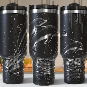 May include: Black travel mug with a handle, featuring a silver illustration of dolphins leaping from ocean waves under a starry sky. The mug has a black lid and handle. The Inkbard logo is visible.