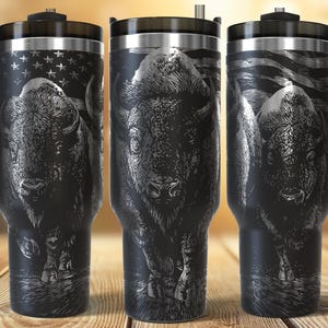 Può includere: Tazze da viaggio nere con una dettagliata illustrazione di un bisonte e un design a bandiera americana. Ogni tazza ha un manico e un coperchio neri. Il disegno è inciso sulla superficie nera, creando un contrasto sorprendente.