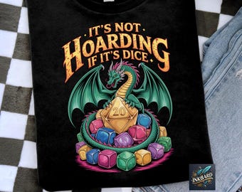 Op de afbeelding: Zwart T-shirt met een groene draak die zich rond een gouden dobbelsteen met het nummer 20 wikkelt. De draak heeft een roze en rode kam, vleugels en een staart. De tekst op het shirt luidt: "Het is geen hamsteren als het dobbelstenen zijn."