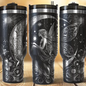 May include: Black travel tumbler with a silver fairy design. The design features a fairy holding a star, surrounded by stars, moons, and floral elements. The tumbler has a black handle and lid.