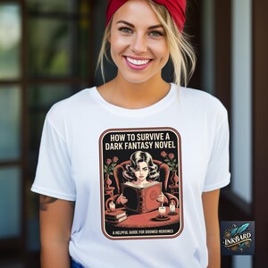 A smiling woman wearing a white t-shirt with a graphic design of a woman reading a book.