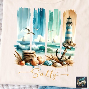 Op de afbeelding: Een beige T-shirt met een aquarel-illustratie van een vuurtoren, anker, schelpen en touw. De tekst "Salty" is in gouden letters onder de illustratie geschreven.