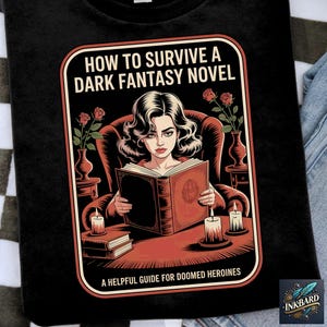May include: Black t-shirt featuring a vintage-style illustration. The design includes a woman reading a book, candles, and roses, with the text "HOW TO SURVIVE A DARK FANTASY NOVEL" and "A HELPFUL GUIDE FOR DOOMED HEROINES".