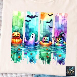 May include: A cream-colored t-shirt featuring a watercolor design of Halloween characters. The design includes a jack-o'-lantern, a ghost, and pumpkins with witch hats, all floating in water with bats and a sun. The design is colorful and whimsical.