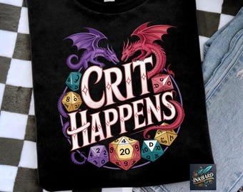 Op de afbeelding: Zwart T-shirt met de tekst "CRIT HAPPENS" en een ontwerp van twee draken, één paars en één rood, tegenover elkaar. Het ontwerp bevat dobbelstenen, zoals een D20, en een cirkelvormige rand. Het shirt is gemaakt van zacht materiaal.