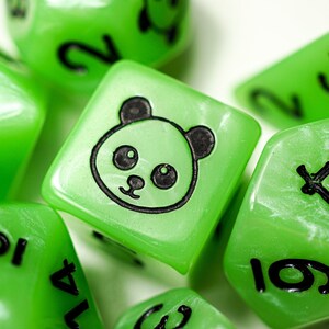 May include: A set of green dice with black numbers and a panda face design. The dice are made of a translucent material with a pearlescent finish.