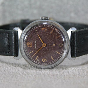 May include: A vintage wristwatch with a brown face and gold-colored hands and numbers. The watch has a black leather band and says "ПОБЕДА" on the face.