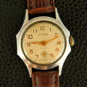 May include: A silver wristwatch with a white face and black leather band. The watch face has black Roman numeral hour markers and a gold second hand. The watch face also has the word "Восток" printed on it.
