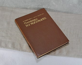 Könnte beinhalten: Ein braunes, ledergebundenes Buch mit goldenen Lettern auf dem Einband. Der Titel lautet "Словарь нумизмата", was mit "Wörterbuch der Numismatik" übersetzt werden kann.