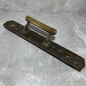 Könnte beinhalten: Antike Türgriff aus Messing mit einer langen, rechteckigen Platte und einem dekorativen Schlüsselloch. Der Griff ist aus einem Stück Metall gefertigt und hat ein schlichtes, elegantes Design.
