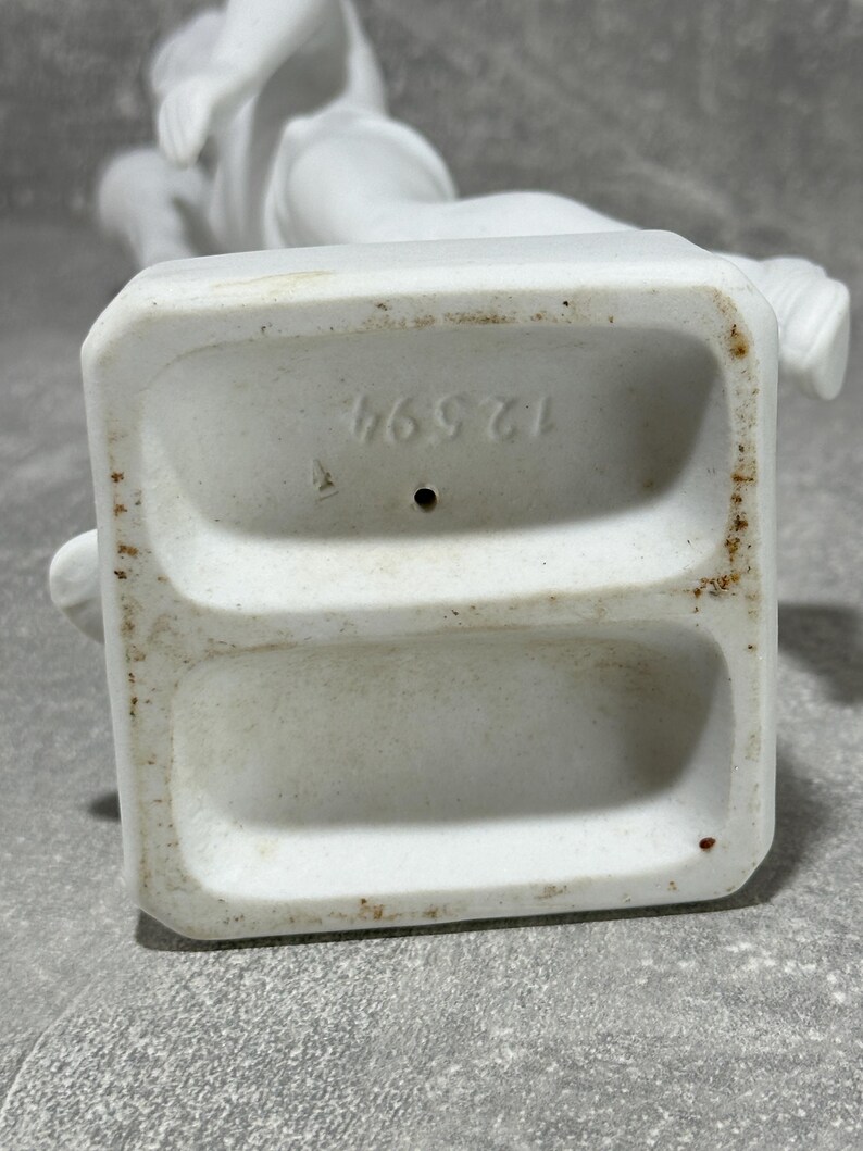 May include: White porcelain statue base with number 46571 imprinted. The base has two recessed areas.  The statue is of a classical style figure. The porcelain is matte white with some minor discoloration.