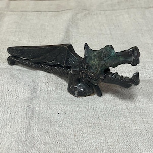 May include: A black metal dragon nutcracker with green accents. The dragon has wings and a long tail. The nutcracker is open, ready to crack nuts.