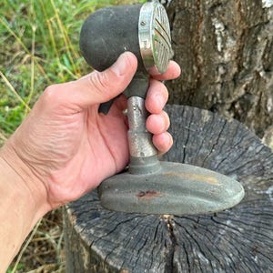 Puede incluir: Micrófono vintage con una cabeza redondeada gris oscuro y una rejilla plateada. El micrófono tiene una base y un tallo plateados. El micrófono se sostiene en una mano sobre un fondo natural.