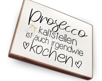 May include: White wooden sign with black text that reads "Prosecco kaltstellen ist auch irgendwie kochen" with a heart symbol on either side of the text. Two glasses of prosecco are depicted above the text.