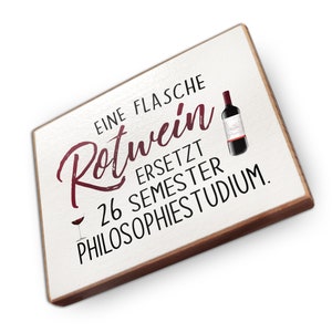Könnte beinhalten: Ein weißes Holzschild mit braunem Rahmen trägt die Aufschrift "Eine Flasche Rotwein ersetzt 26 Semester Philosophiestudium."  Auf dem Schild sind ein Glas Rotwein und eine Flasche Rotwein abgebildet.