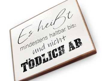 May include: A rectangular wooden sign with a white surface and brown edges. The sign features black text in various fonts, including the words "Es heißt" and "TÖDLICH AB". The sign is angled slightly.