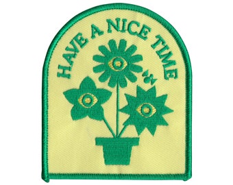 May include: Green embroidered patch with a yellow background. The patch features three stylized flowers in a pot with the text "HAVE A NICE TIME" around the flowers.