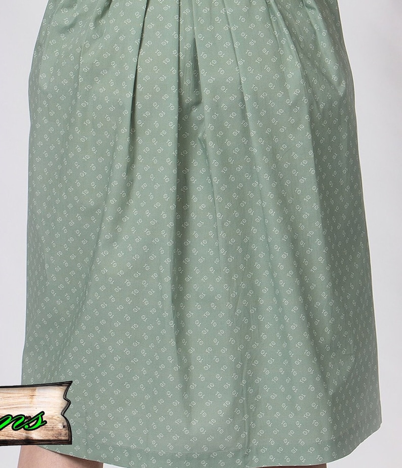 May include: A sage green skirt with a repeating white floral pattern. The skirt has pleats at the waist and a slight A-line shape. The fabric appears to be cotton or a similar lightweight material.