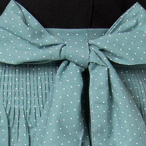 K&ouml;nnte beinhalten: Eine blaugr&uuml;ne Sch&uuml;rze mit wei&szlig;en Punkten und einer passenden Schleife, die in der Taille gebunden ist.