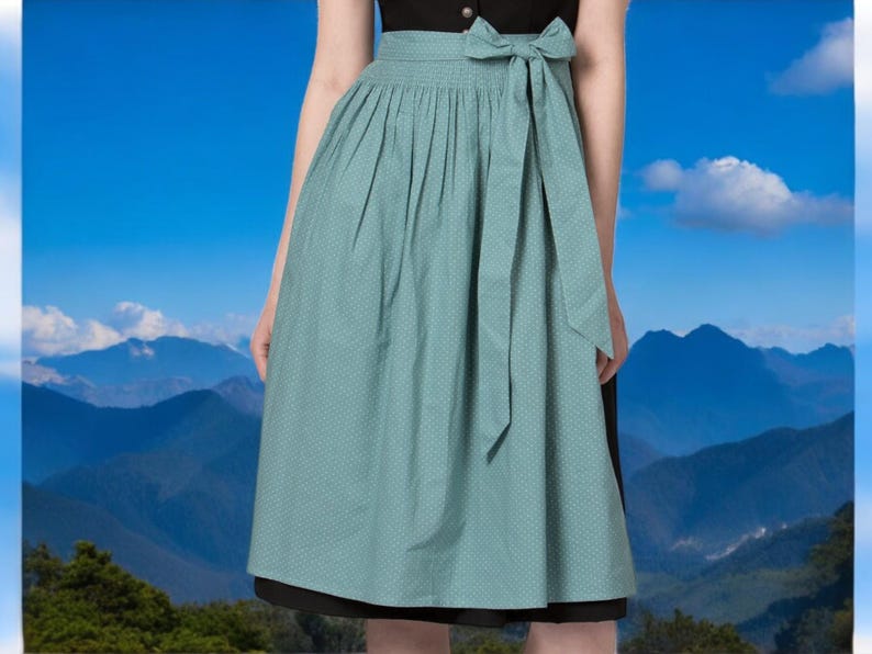 K&ouml;nnte beinhalten: Ein blaugr&uuml;nes Dirndl mit wei&szlig;em Tupfenmuster und einer wei&szlig;en Schleife. Das Dirndl hat eine schwarze Sch&uuml;rze und wird von einer Person getragen, die vor einer Bergkette steht.