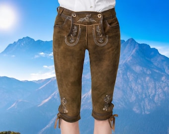 May include: Brown leather shorts with embroidered floral details and gold buttons. The shorts have a traditional style and are worn against a backdrop of mountains.