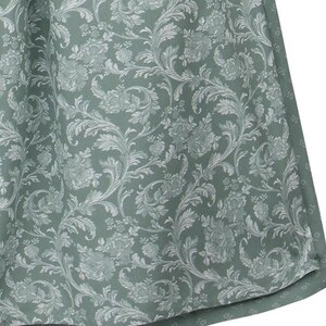 May include: Close-up of a fabric with a repeating floral pattern. The fabric has a sage green background with a white, detailed floral design. The pattern includes flowers, leaves, and swirling vines, creating a classic, elegant look. The fabric appears to be a curtain or drapery.