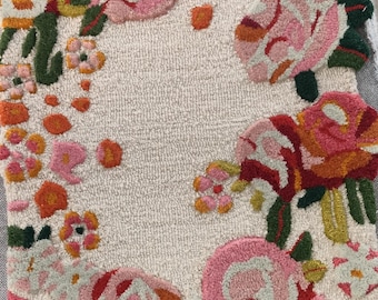 Puede incluir: Una alfombra blanca con un diseño floral con flores rosas, rojas, naranjas y verdes. La alfombra tiene una superficie texturizada y esponjosa.