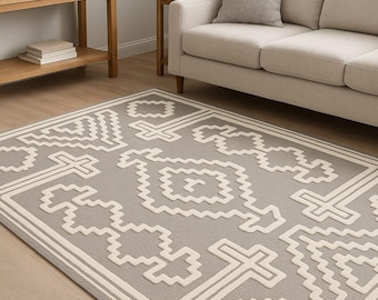 Pode incluir: Um tapete retangular cinza com um padrão geométrico branco. O tapete, com uma borda, está colocado sobre um chão de madeira. A cena é uma sala de estar, com um sofá e uma mesa lateral visíveis.