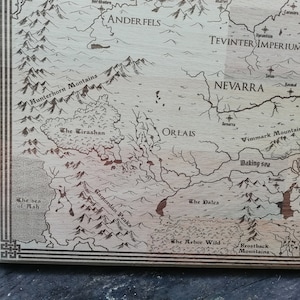 May include: A light brown wooden laser-engraved map of Thedas, featuring various regions including Ferelden, Orlais, Tevinter Imperium, and Nevarra.  The detailed map showcases mountains, rivers, and seas, with region names clearly labeled.  The wood grain is visible, adding to the rustic aesthetic.  This decorative map is perfect for fantasy fans and gamers.