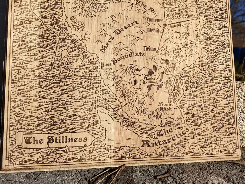 May include: A laser-engraved wooden map features a fantasy world with names like Merz Desert, Bomidlats, and The Antarctica.  The map's style is reminiscent of antique cartography, with detailed coastlines and landmasses.  The color palette is monochromatic, showcasing various shades of brown on the wood.  The text is clearly legible, adding to the map's intricate detail.  The map's overall aesthetic is rustic and charming, suitable for tabletop gaming or home decor.