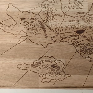 May include: A laser-engraved wooden map features various regions, including Barren Lands, Ruberios, Sillrosso, Ingrasia, Farmas, Brumund, Various Western States, Sarion, and Ulgreisia.  The light brown wood grain is visible through the engraved lines.  The map's style is reminiscent of fantasy or role-playing game settings.  The names of the regions are clearly visible, engraved in a stylized font.  The map's design includes mountains, forests, and bodies of water, all rendered in a detailed, hand-drawn style.  The overall aesthetic is rustic and charming.