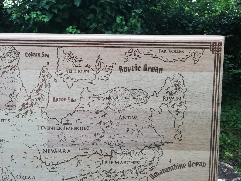 May include: A light brown wooden engraved map of a fantasy world. The map features various geographical features such as oceans, seas, mountains, forests, and countries with names like 'Seheron,' 'Antiiva,' 'Par Vollen,' 'Tevinter Imperium,' and 'Free Marches.' The map has a decorative border and is a unique piece for tabletop gaming or home decor.