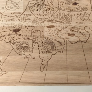 May include: A light brown wooden laser-engraved fantasy world map features various kingdoms and regions, including Ruberios, Sillrosso, Ingrasia, Dwargon, Farmas, Tura Tempest Federation, Brumund, Various Western States, Sarion, Ulgreisia, Fulbrosia, Eurazania, and Jistraru.  The map's intricate details include mountains, forests, and rivers, creating a detailed and immersive fantasy setting.  The names of the regions are clearly engraved, enhancing the map's readability and visual appeal. The map's rustic wooden texture adds to its charm and makes it suitable for tabletop gaming or as a decorative piece.