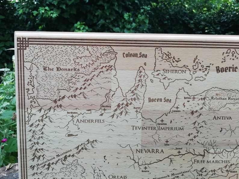 May include: A laser-engraved wooden map features various regions, including The Donarks, Anderfels, Seheron, Antiva, Tevinter Imperium, and Nevarra.  The map is bordered by a decorative frame and showcases detailed geographical features like mountains and seas, labeled with names like Colean Sea and Rocen Sea. The light-brown wood provides a natural contrast to the darker brown engraved lines.  The style evokes fantasy or role-playing game settings.
