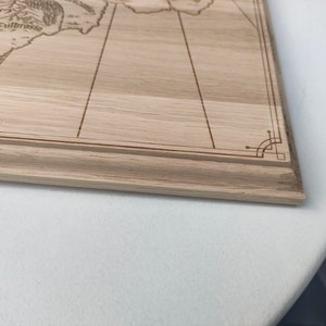 May include: Close-up view of a light brown wooden board with a laser-engraved map. The map features lines, text including 'Fulbrose', and decorative corner details. The board has a light wood grain and a simple frame. The image shows the bottom right corner of the board.
