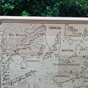 May include: Light brown wooden laser-engraved fantasy map featuring various regions, seas, and mountain ranges.  The Donarks, Ander Fels, Tevinter Imperium, and Nevarra are among the labeled regions.  The Colean Sea and Rocen Sea are also depicted.  The map's border is accented with a decorative frame.  The style evokes classic fantasy game maps.