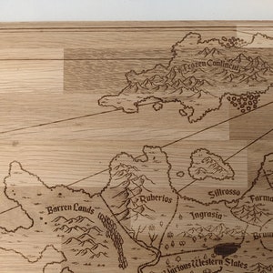May include: A light brown wooden laser-engraved fantasy map features various regions including Frozen Continent, Barren Lands, Ruberios, Sillrosso, Ingrasia, Farmas, Brunnund, and the Jarious Western States.  The map's intricate details include mountains, forests, and coastlines, creating a detailed and visually appealing design. The names of the regions are clearly labeled, enhancing the map's readability and providing a clear geographical context. The overall aesthetic is reminiscent of classic fantasy map designs, making it suitable for tabletop gaming or decorative purposes.
