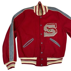 May include: A red varsity jacket with gray leather sleeves and accents. The jacket features a large letter "S" patch with a basketball graphic. The collar, cuffs, and waistband have striped detailing. The jacket has a button-up front and two front pockets.