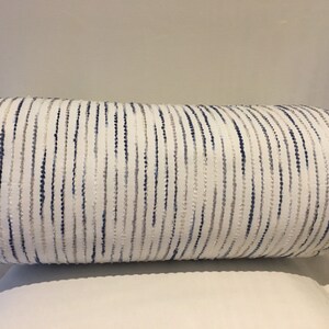 May include: A white cylindrical cushion with blue and grey stripes. The stripes are made of small, raised dots.