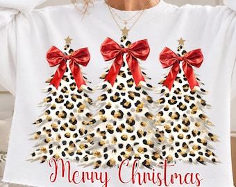May include: A white long-sleeve sweatshirt featuring a graphic of three Christmas trees with a black and gold leopard print pattern. Each tree is topped with a gold star and a large red bow. The text Merry Christmas is printed in red script.